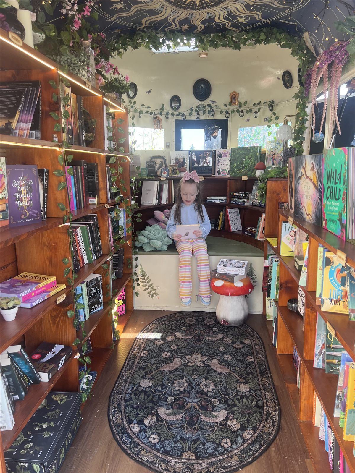 Mila inside the Willow Wisp Books trailer, surrounded by bookshelves and fairy lights