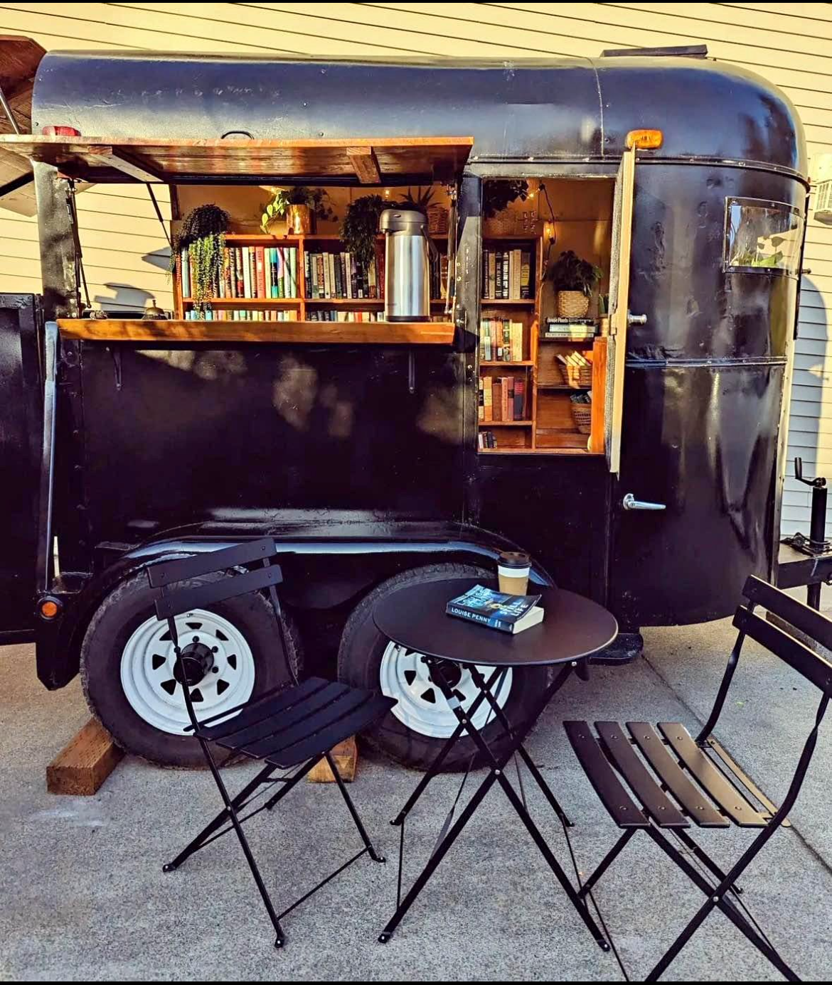 The Willow Wisp Books trailer — a converted horse trailer with wooden bookshelves, plants, and a bistro table
